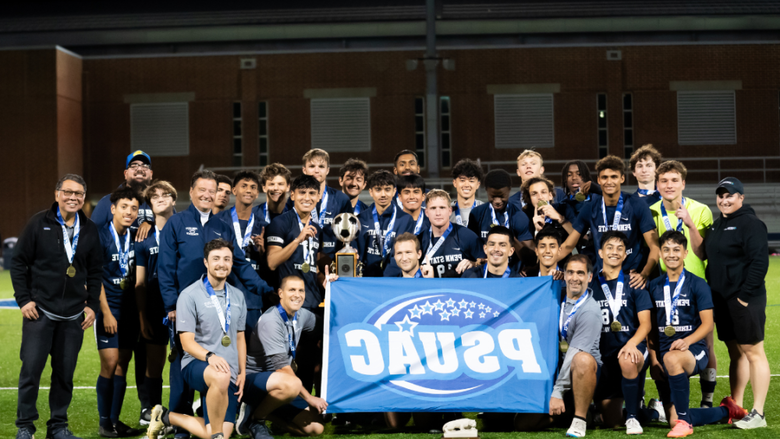 male soccer players pose for a group photo on a soccer field with a blue flag